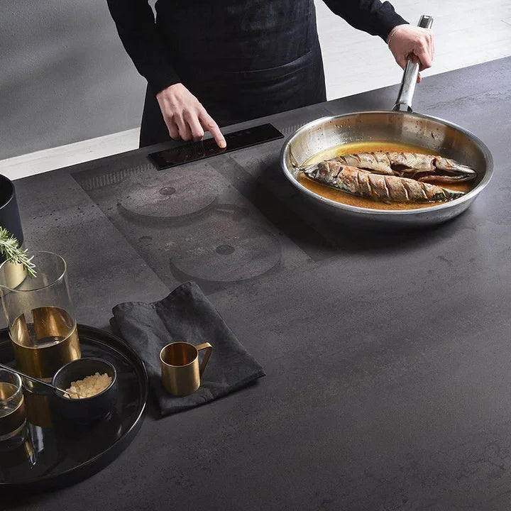 Cocinero usando el cooktop Invisacook de inducción invisible sobre encimera negra con sartén