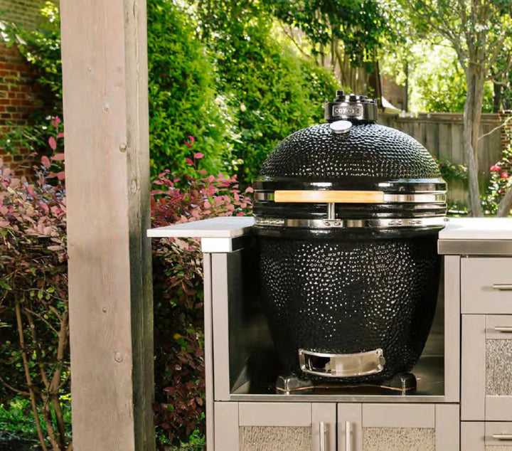 Asador de carbón Coyote C1CHCS negro empotrado en isla de exterior rodeado de vegetación