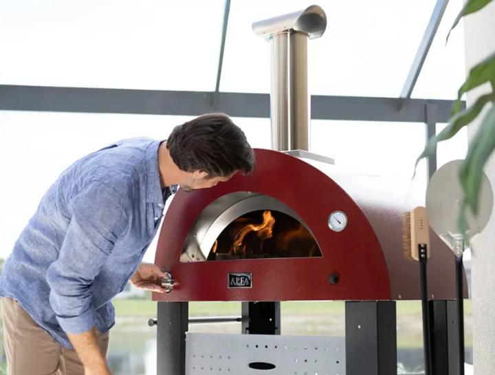 Hombre usando el horno de pizza a gas Alfa Forni encendido en una terraza exterior