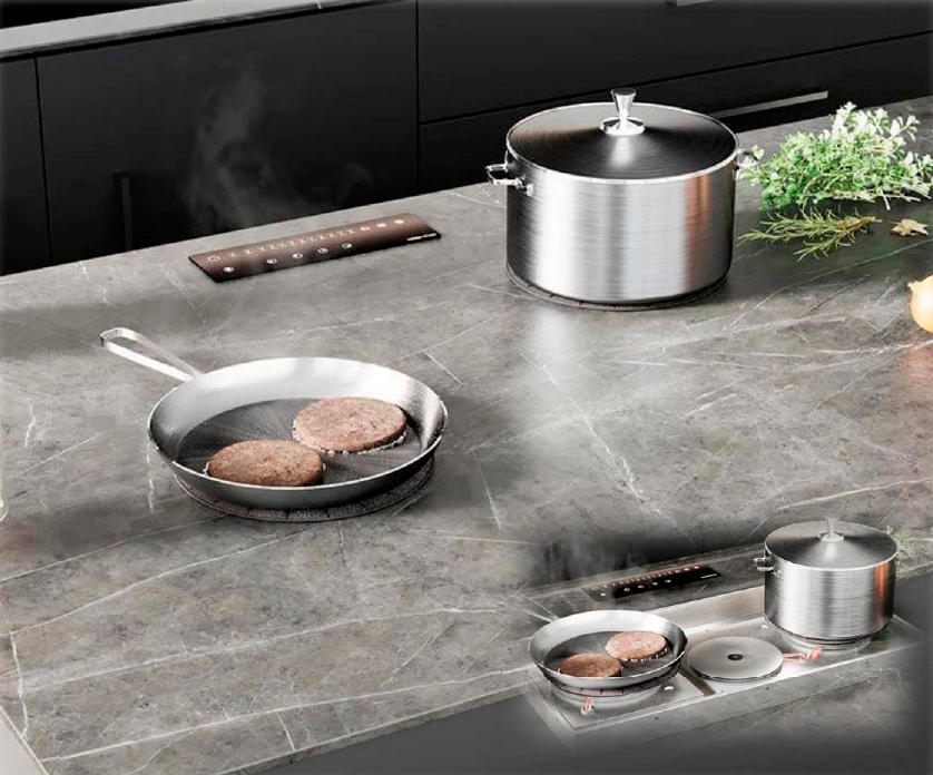 Cooktop Invisacook de inducción invisible cocinando ollas y sartén sobre encimera de piedra