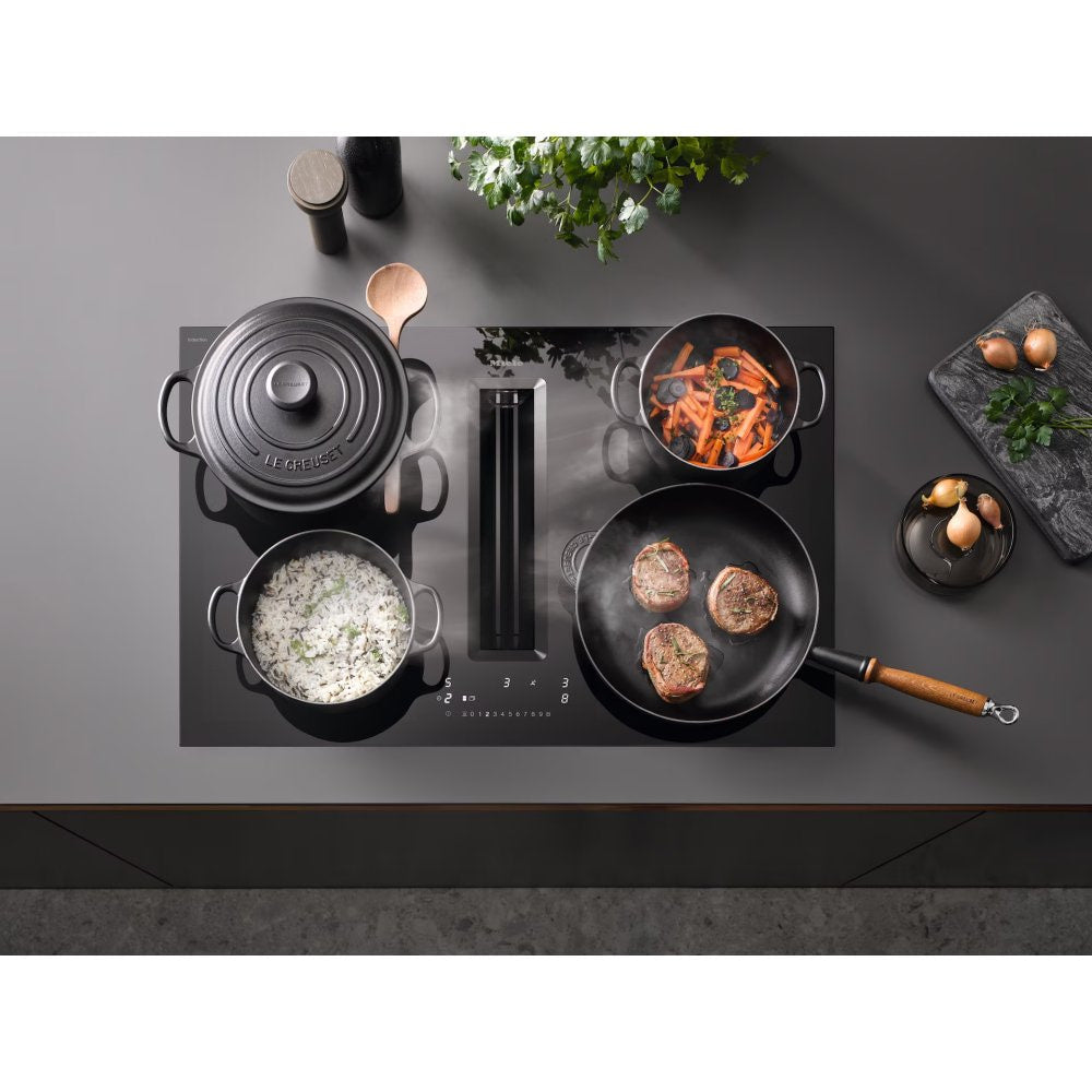 Placa de inducción con extractor integrado Miele KMDA 7676-1 FL BlackPerfection cocinando con ollas y sartenes, vapor absorbido por la ranura central, ambiente de cocina
